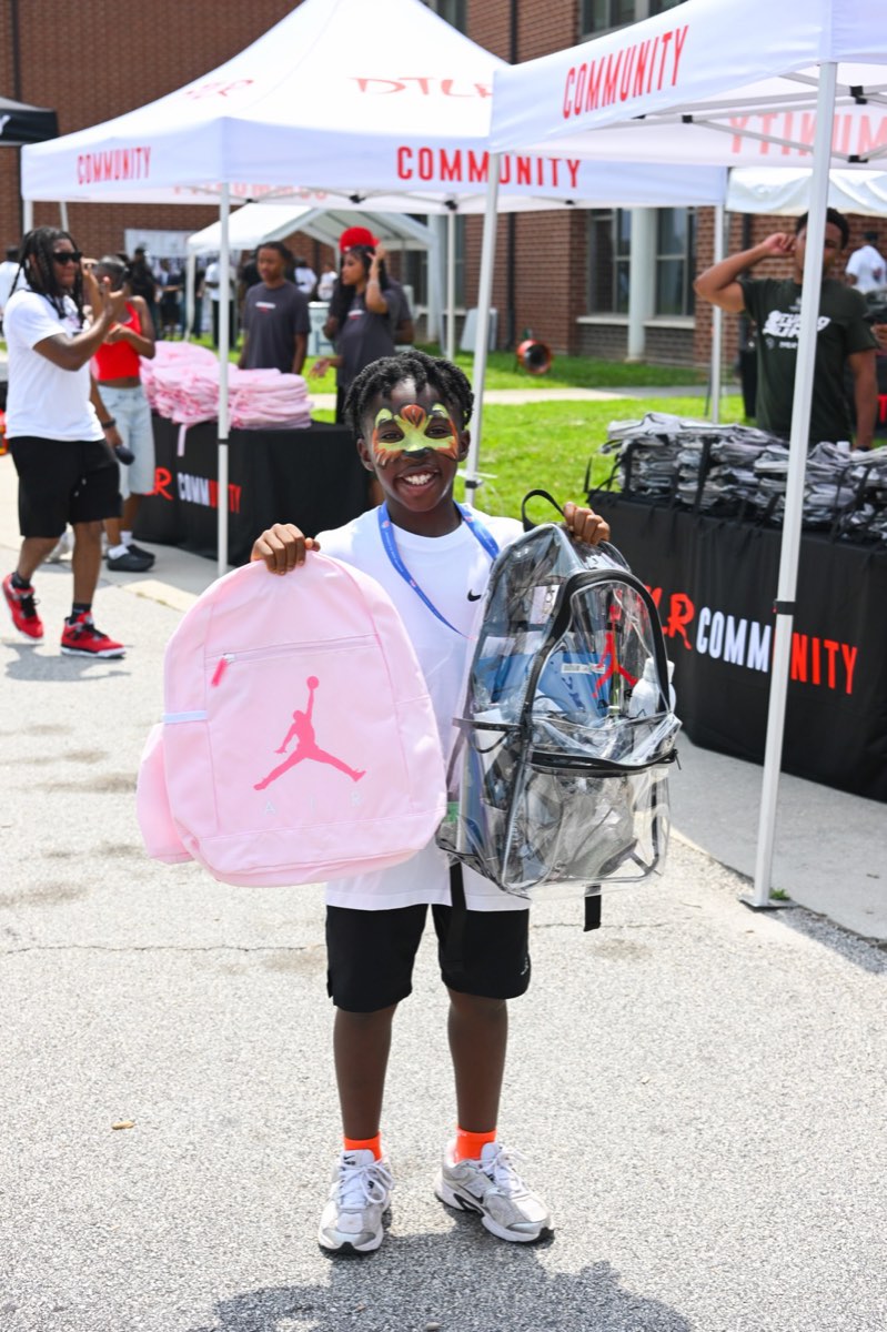 Child holding up a new backpack at the Turbo Day 2026 school supply giveaway