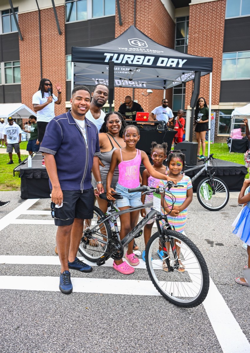 Turbo handing a new bike to a family at the Turbo Day 2026 bike giveaway
