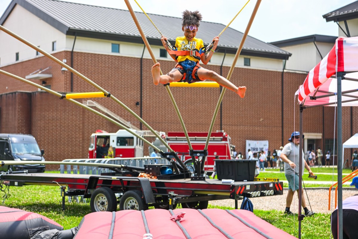 Child leaping high on the bungee trampoline with a fire truck behind at Turbo Day 2026